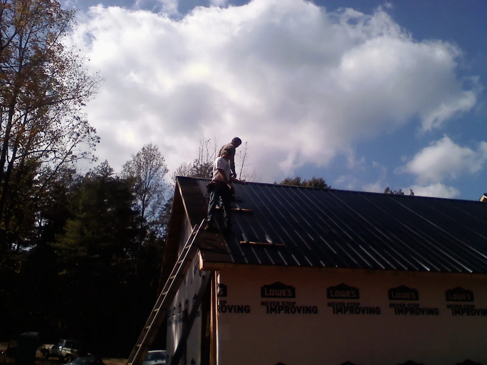 Roofer fastening dark metal panels high against a cloudy sky, from a Roof Inspection job in Deerfield Beach