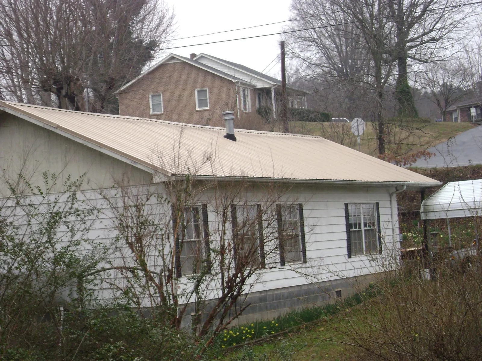 Tan metal roof on a white sided house set into a hillside — Commercial Roofing by Roofing Brothers in Deerfield Beach